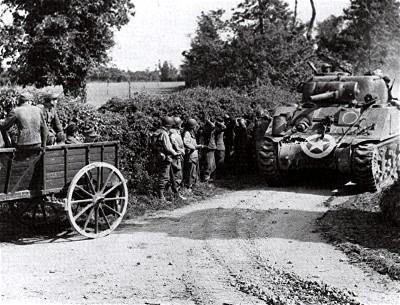 M4 Sherman Tank of the 70th Tank Battalion in
Normandy passes GIs and a wagon-load of German POWs.